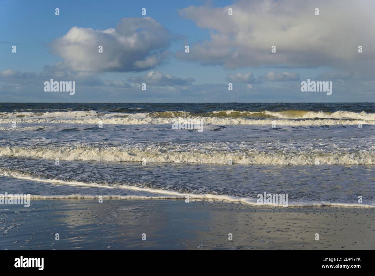 Vagues sur une plage de sable avec formation de mousse, ciel bleu avec des nuages profonds d'enflure (cumulus) au-dessus de la mer du Nord, Norderney, îles de la Frise orientale, Lower Banque D'Images