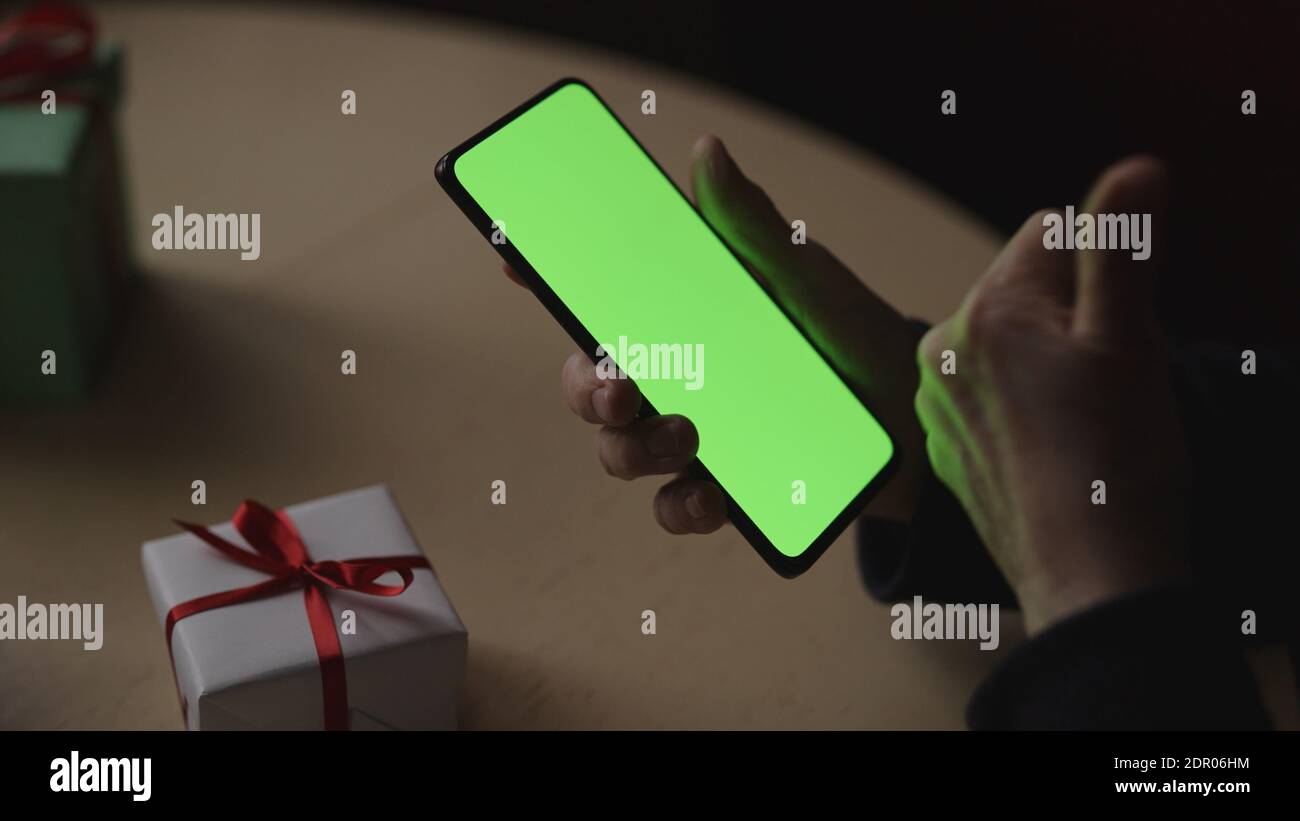 les vieilles mains des femmes tiennent un smartphone avec un écran vert et célèbrent les fêtes en discutant avec la famille, photo large Banque D'Images