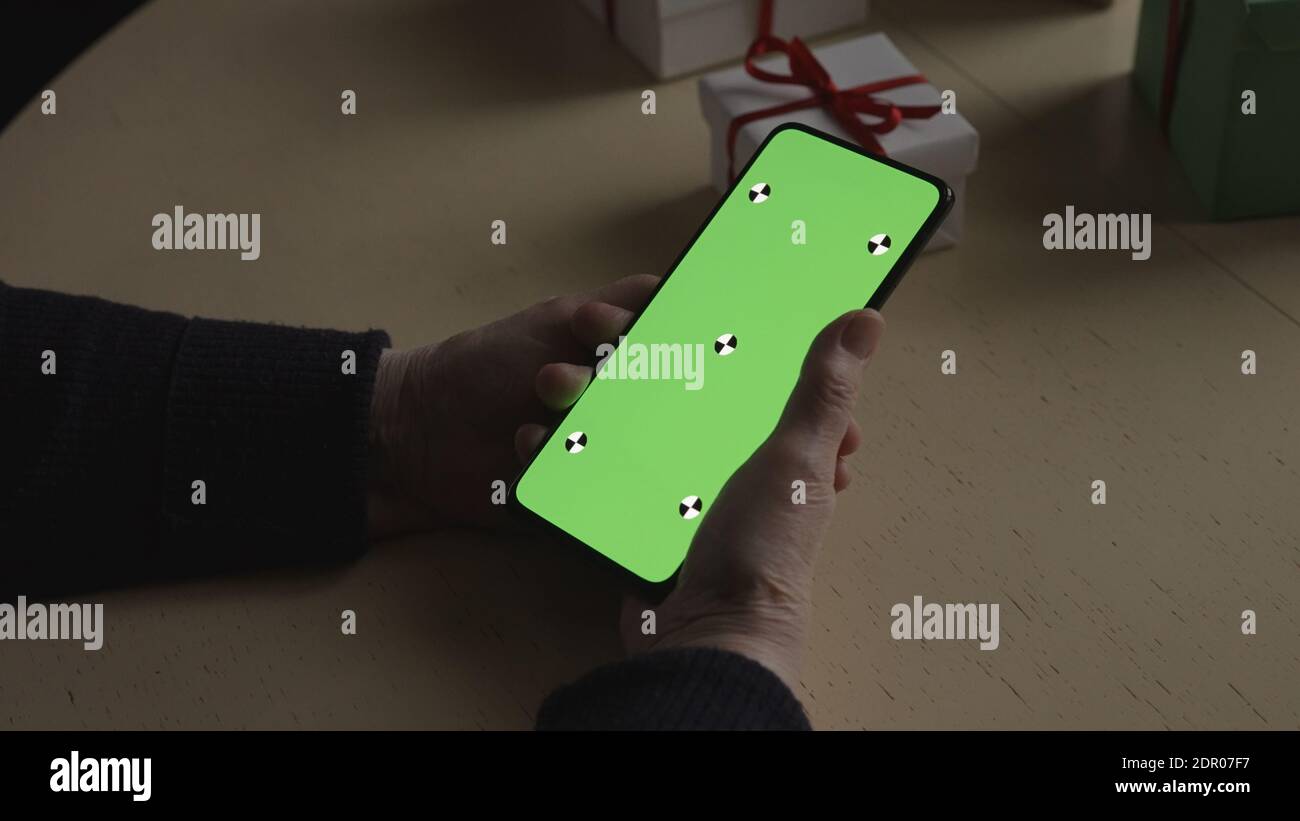 les vieilles mains des femmes tiennent un smartphone avec un écran vert et célèbrent les fêtes en discutant avec la famille, photo large Banque D'Images