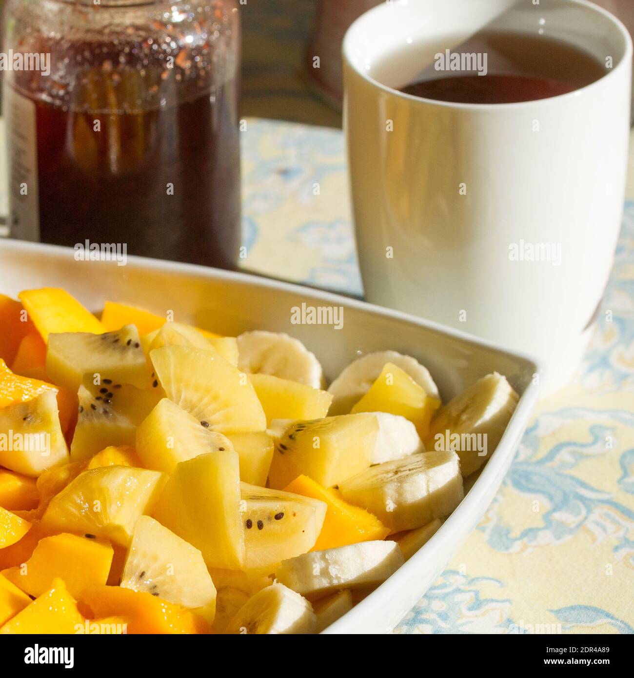Grande assiette de fruits exotiques frais pour le petit déjeuner, mangue, bananes, kiwi doré sur une table avec thé et confiture de fraises Banque D'Images