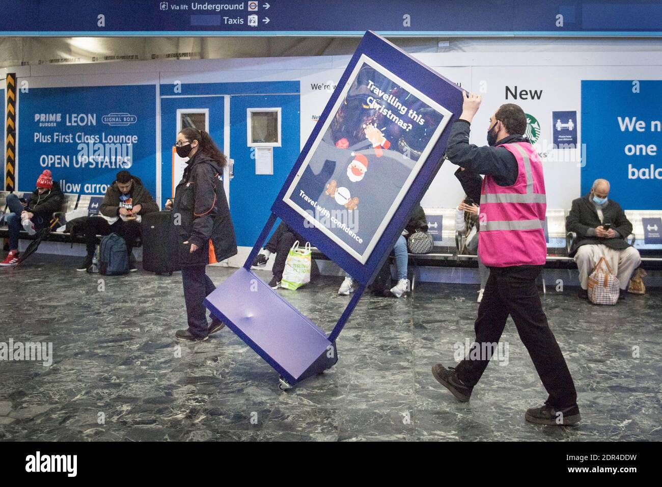 Un employé de la gare retire un panneau « Voyager à Noël » de la gare d'Euston, à Londres, Le public étant invité à respecter les directives du gouvernement après que le Premier ministre Boris Johnson ait annoncé samedi que, depuis les régions du Sud-est actuellement dans le niveau 3, le dimanche sera transféré dans un nouveau niveau 4 pendant deux semaines Ð de retour aux règles de verrouillage de novembre, après que les scientifiques ont averti de la propagation rapide du nouveau coronavirus variant. Banque D'Images