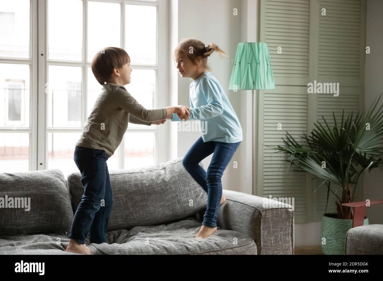 Un petit garçon et une fille surjoyés se tenant les mains, sautant sur un canapé Banque D'Images