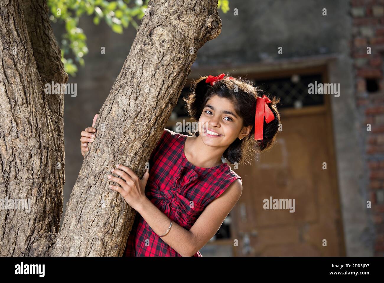 Petite fille regardant d'un arbre de cacher et de chercher à village Banque D'Images