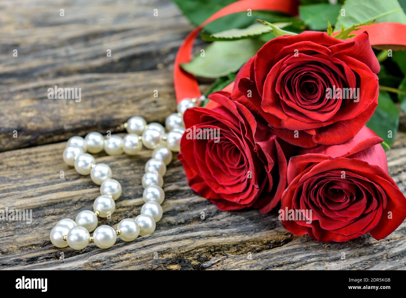 Trois roses rouges et une chaîne de perles sur une ancienne table en bois avec un espace de copie pour le texte. Mise au point sélective. Banque D'Images