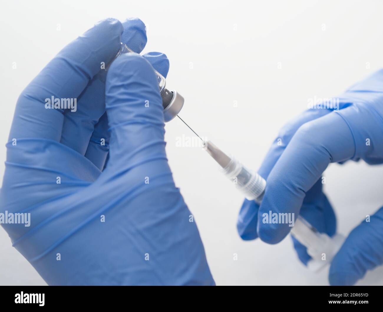Mains dans des gants en caoutchouc bleu contenant une seringue et un flacon médicaux Gros plan sur fond blanc Banque D'Images