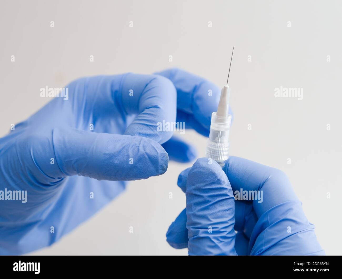 Mains dans des gants en caoutchouc bleu tenant une seringue médicale en gros plan Arrière-plan blanc Banque D'Images