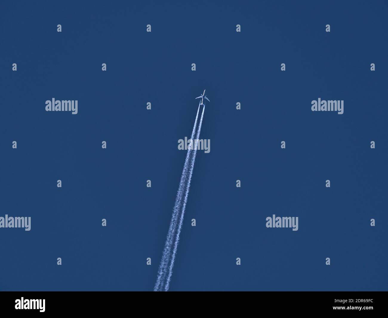 Vue à angle bas d'un avion à deux moteurs volant avec sentier de condensation de couleur blanche dans un ciel bleu clair. Banque D'Images