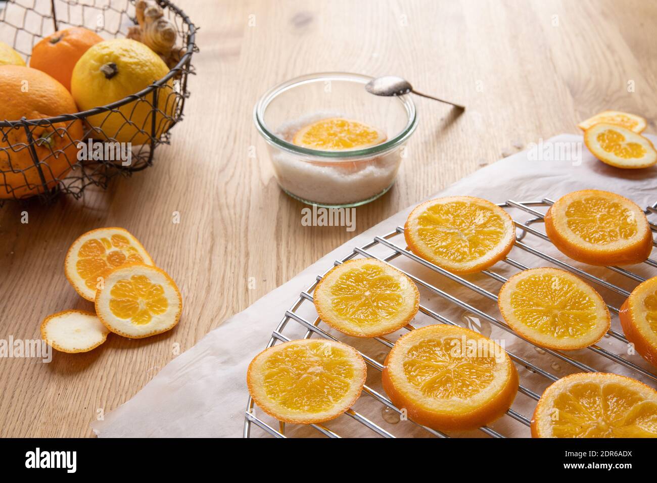 Concept d'oranges confites: Un bol de sucre avec une tranche d'orange et une cuillère, et des tranches d'orange sur un rack un dessus de papier parchemin a sur une table en bois. Banque D'Images