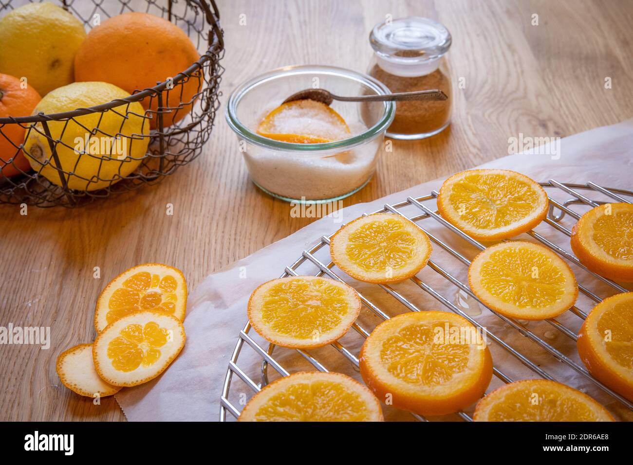 Concept d'oranges confites : un bol de sucre avec une tranche d'orange et une cuillère, un mélange d'épices pour pain d'épice et des tranches d'orange sur une table en bois. Banque D'Images