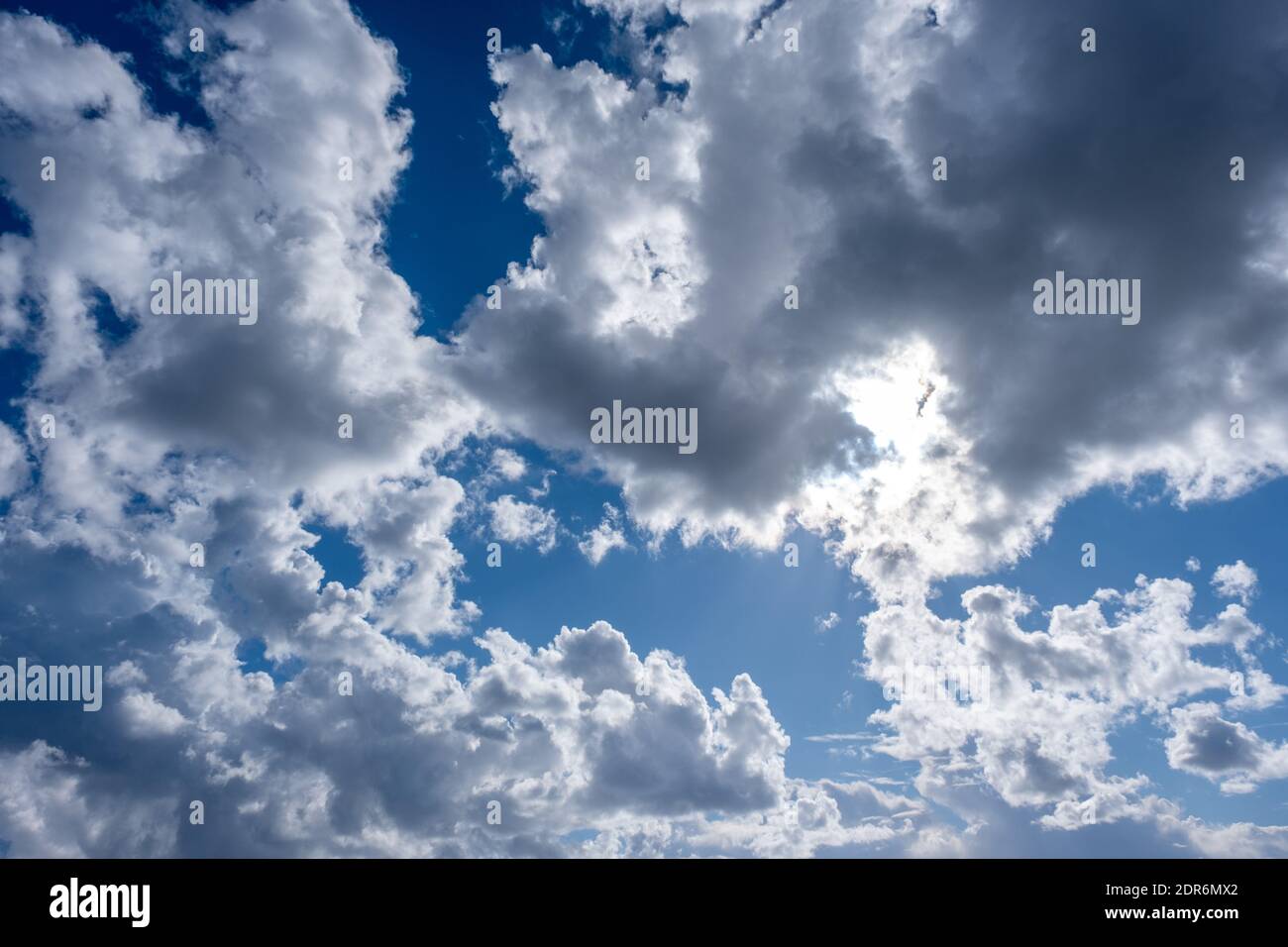 Fond ciel naturel. Nuages gris et blancs moelleux suspendus sur le ciel bleu. Le soleil brille derrière les nuages. Banque D'Images