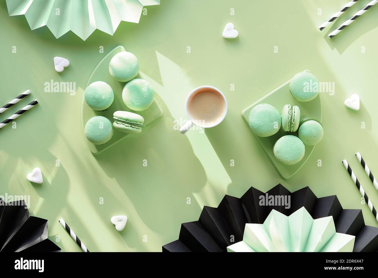 Macarons et café sucrés et savoureux. Pose à plat monochrome créative sur du papier vert menthe. Ventilateurs en papier pliés et pailles en papier strippy. Naturel Banque D'Images