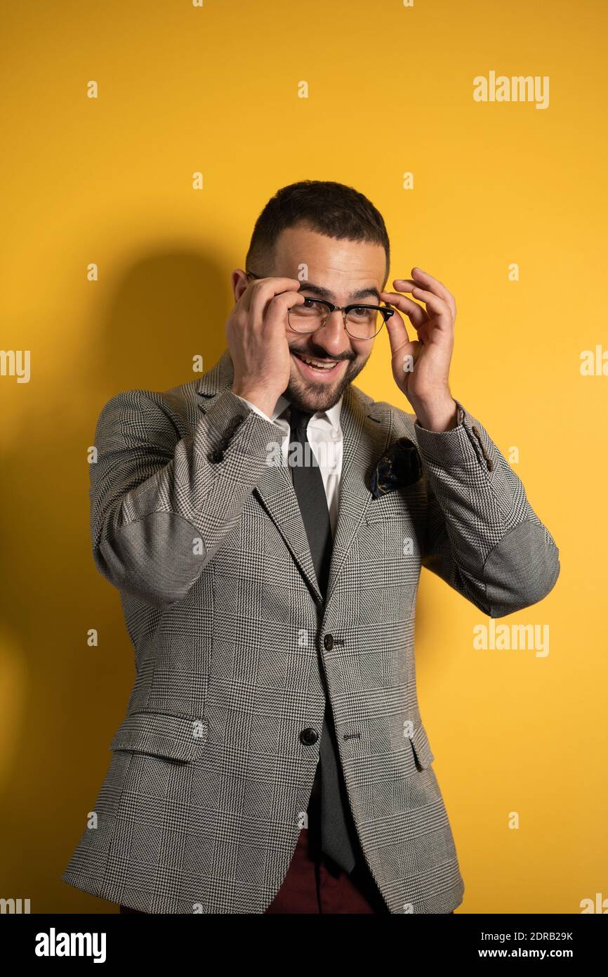 Mettre des lunettes beau sourire élégant homme portant habillé blouson gris avec les deux mains soulevées debout peu isolé latéralement sur jaune Banque D'Images