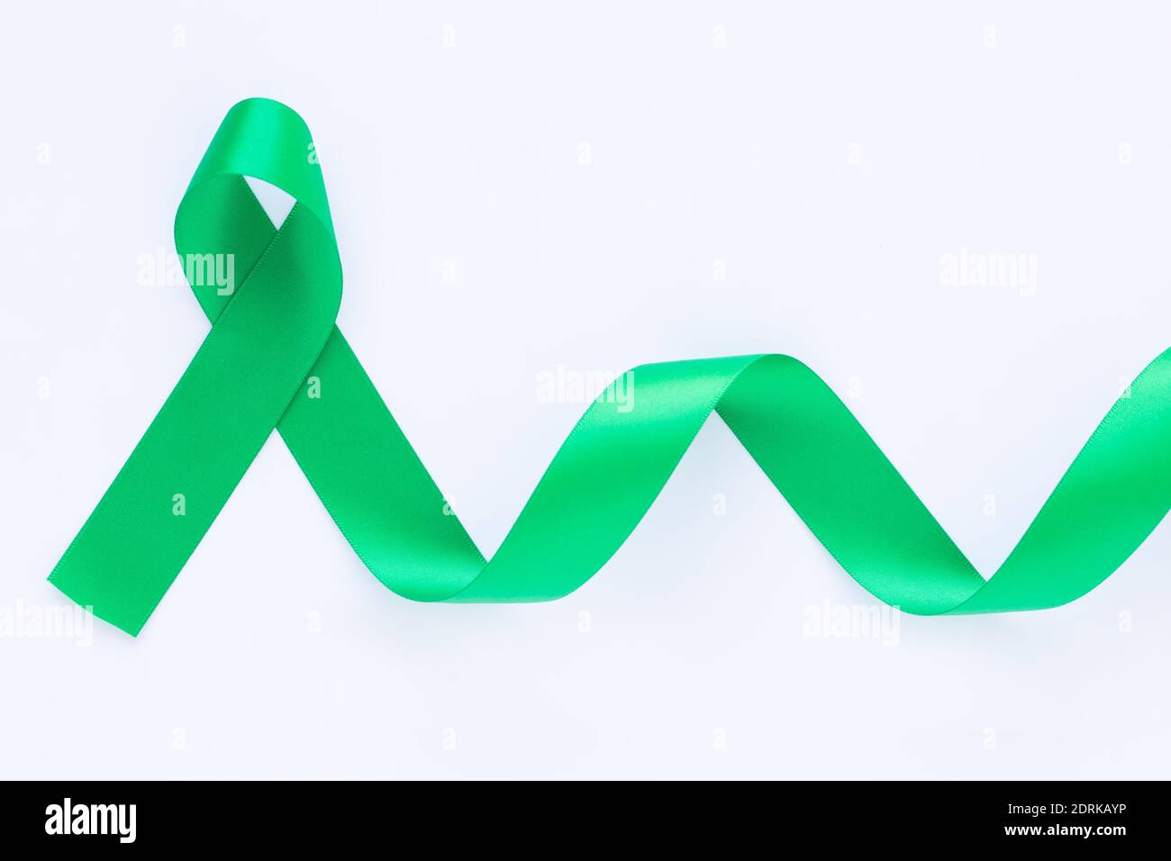 Ruban vert émeraude ou vert jade gondolé sur fond de tissu blanc avec espace de copie, symbole de sensibilisation au cancer du foie, Journée mondiale du cancer. Soins de santé ou Banque D'Images