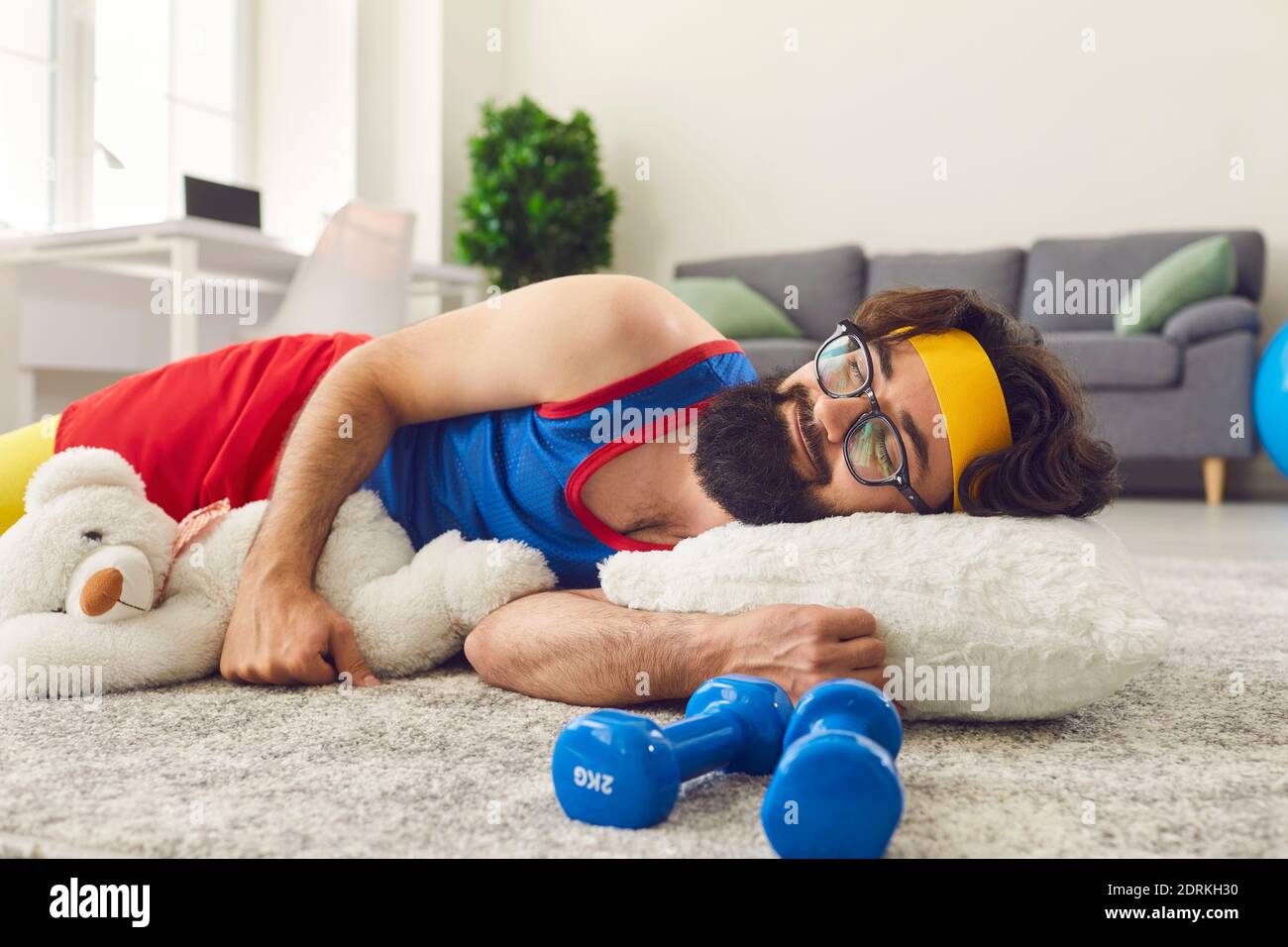 Homme paresseux à barbe allongé sur le sol près des haltères et se nappant au lieu de s'entraîner. Banque D'Images