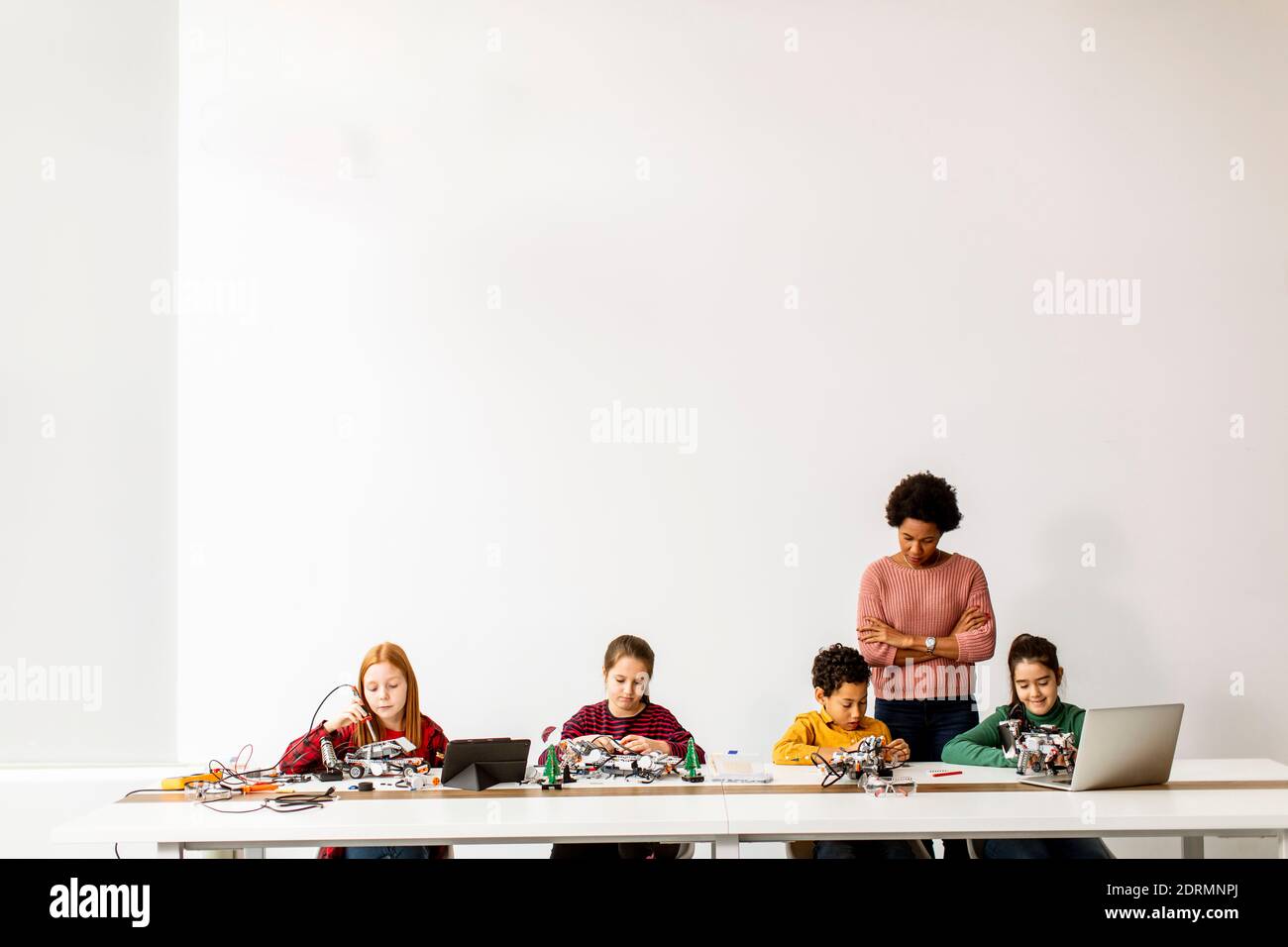 Groupe d'enfants heureux avec leur science féminine afro-américaine professeur avec des jouets électriques de programmation d'ordinateur portable et des robots à la robotique salle de classe Banque D'Images