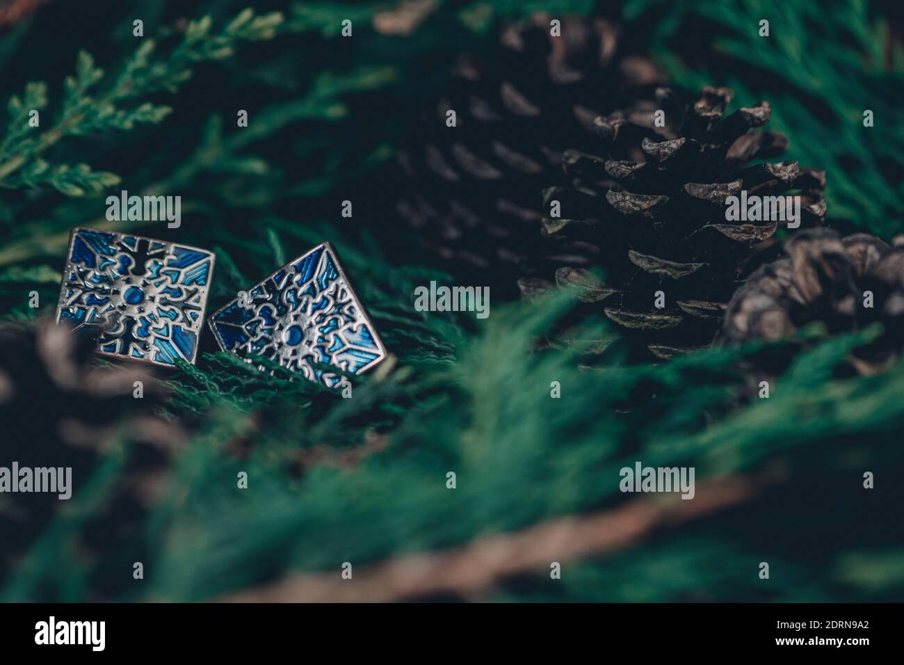 Thame,UK - 25 Nov 2020: Boutons de manchette bleus en argent sur fond vert permanent et pommes de pin, motif flocon de neige sur chaque lien de manchette, bijoux de noël pour hommes Banque D'Images
