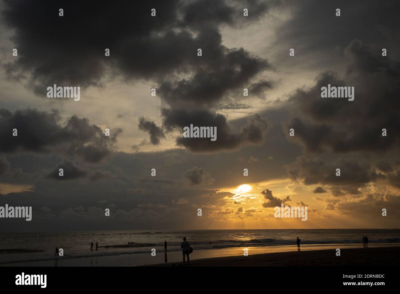 Les surfeurs et les touristes silhouettes sur la côte de l'océan au coucher du soleil rouge Banque D'Images