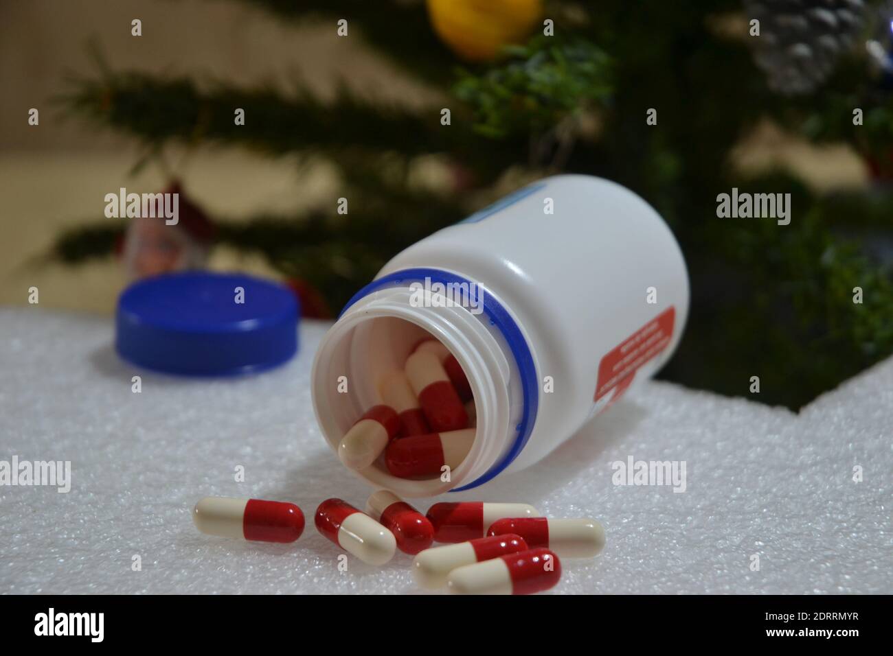 Flacon avec capsules blanches et rouges pour le traitement, avec capuchon bleu sur fond blanc avec un fond d'arbre de Noël Banque D'Images