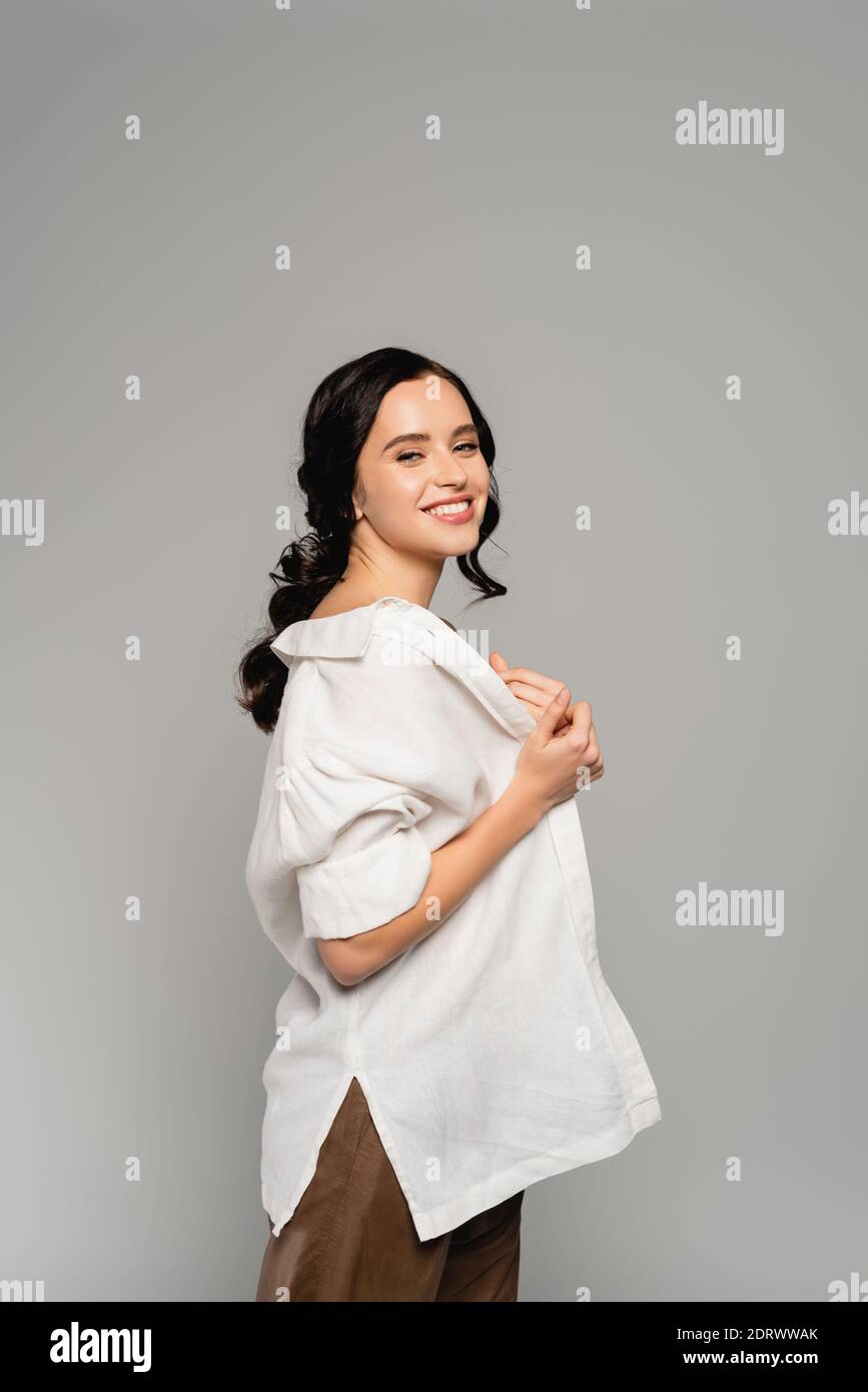 Gaie brune femme regardant l'appareil photo tout en prenant le blanc chemise isolée sur gris Banque D'Images