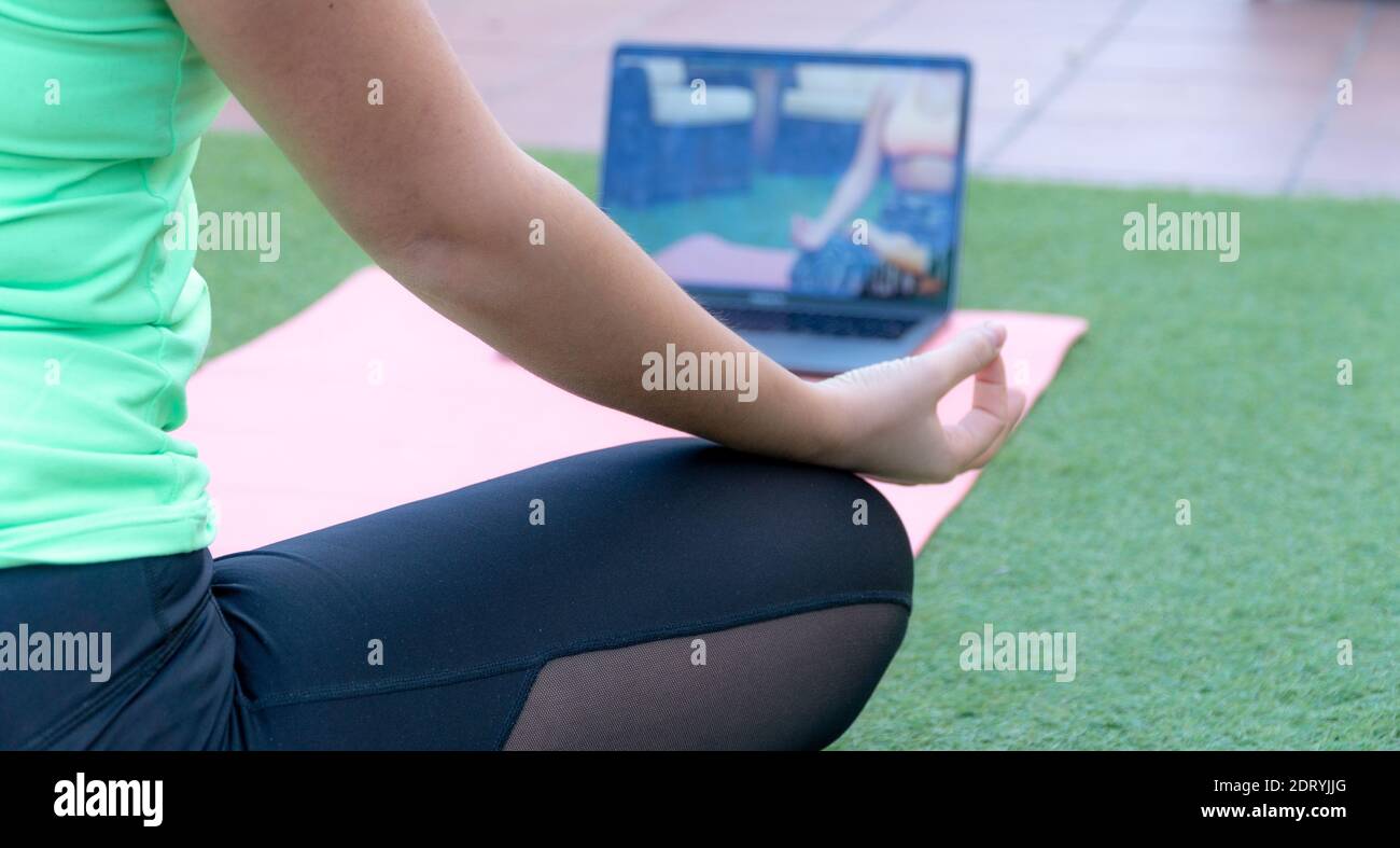 Une femme faisant un cours de yoga en ligne dans le jardin de sa maison. Nous pouvons voir un gros plan de sa jambe droite et de son bras pendant que la femme effectue la méditation Banque D'Images