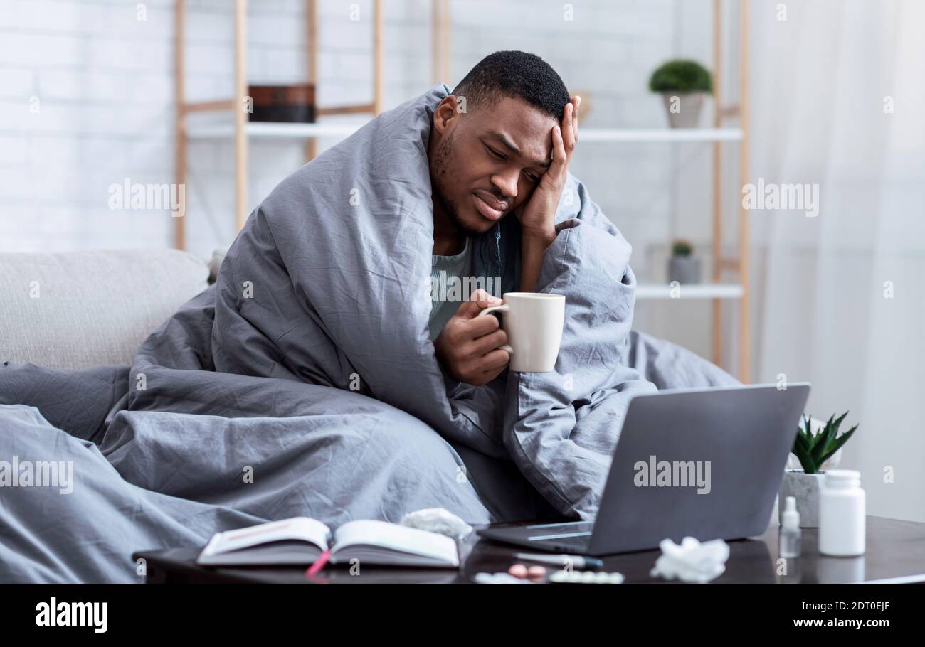 Malade Africain Homme utilisant un ordinateur portable ayant de la fièvre et des maux de tête en intérieur Banque D'Images