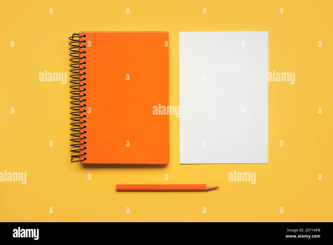 bloc-notes spirale orange avec une feuille de papier blanc et crayon orange sur fond jaune Banque D'Images