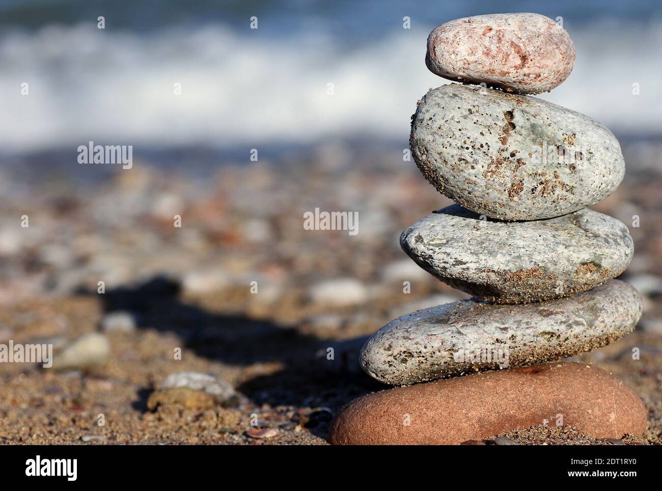 Pierres d'équilibrage: Une pile de pierres colorées équilibrée l'une sur l'autre avec une plage de galets et une vague se brisant sur l'estran en arrière-plan Banque D'Images