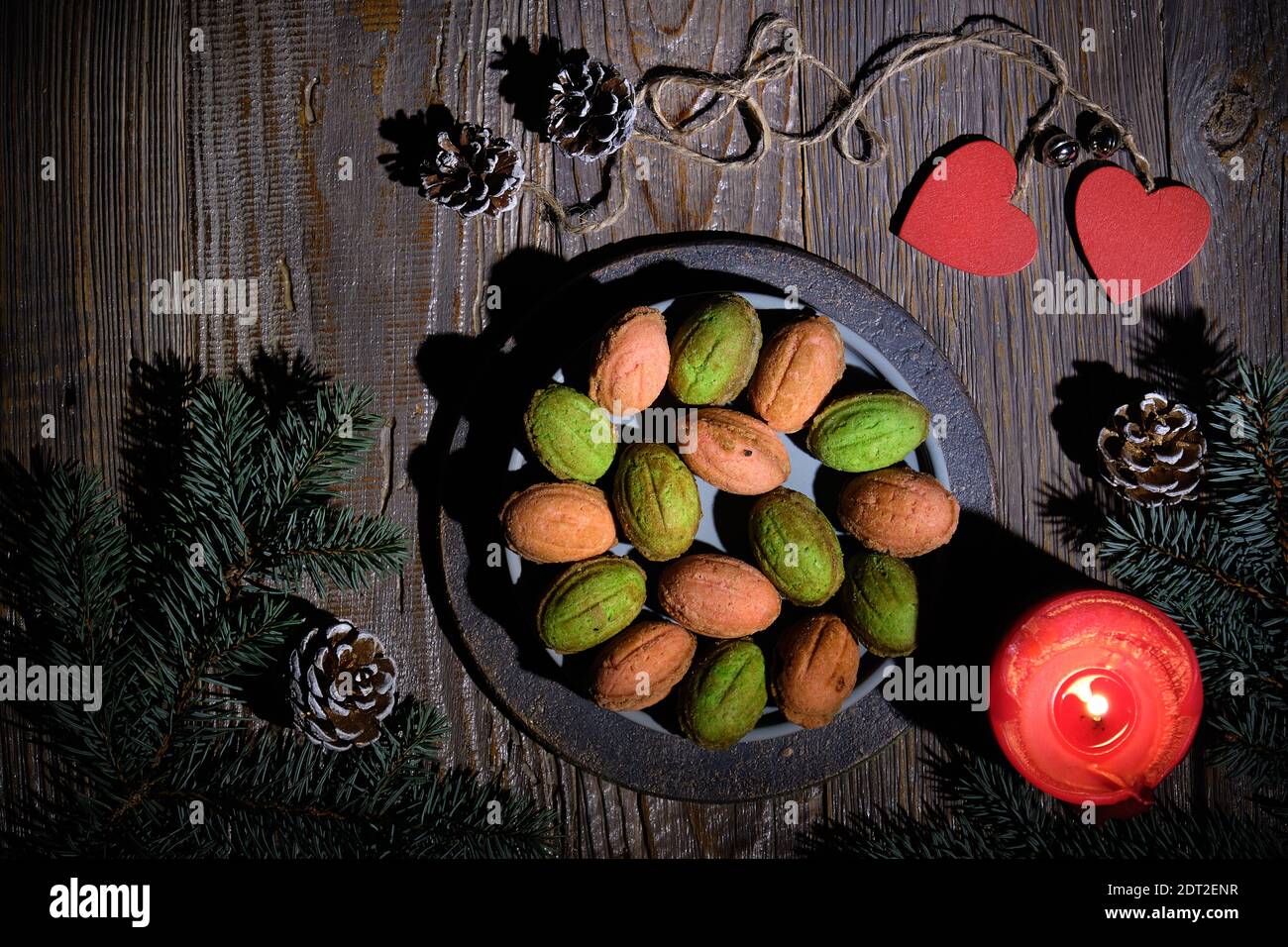 Biscuits aux noix avec Dulce de Leche ou lait condensé. Lumière naturelle, ombres longues. Brindilles de sapin décorées de cônes de pin, d'une bougie rouge et d'un coeur en bois Banque D'Images