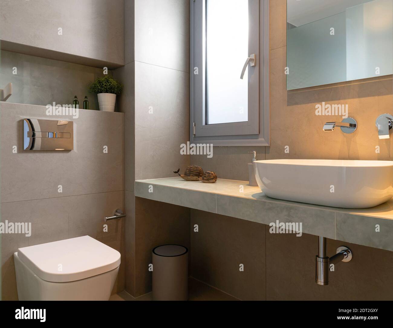 Intérieur de style moderne de petite salle de bains en pierre grise carrelée avec fenêtre, lavabo pour bateau, miroir de lumière arrière, toilettes murales Banque D'Images