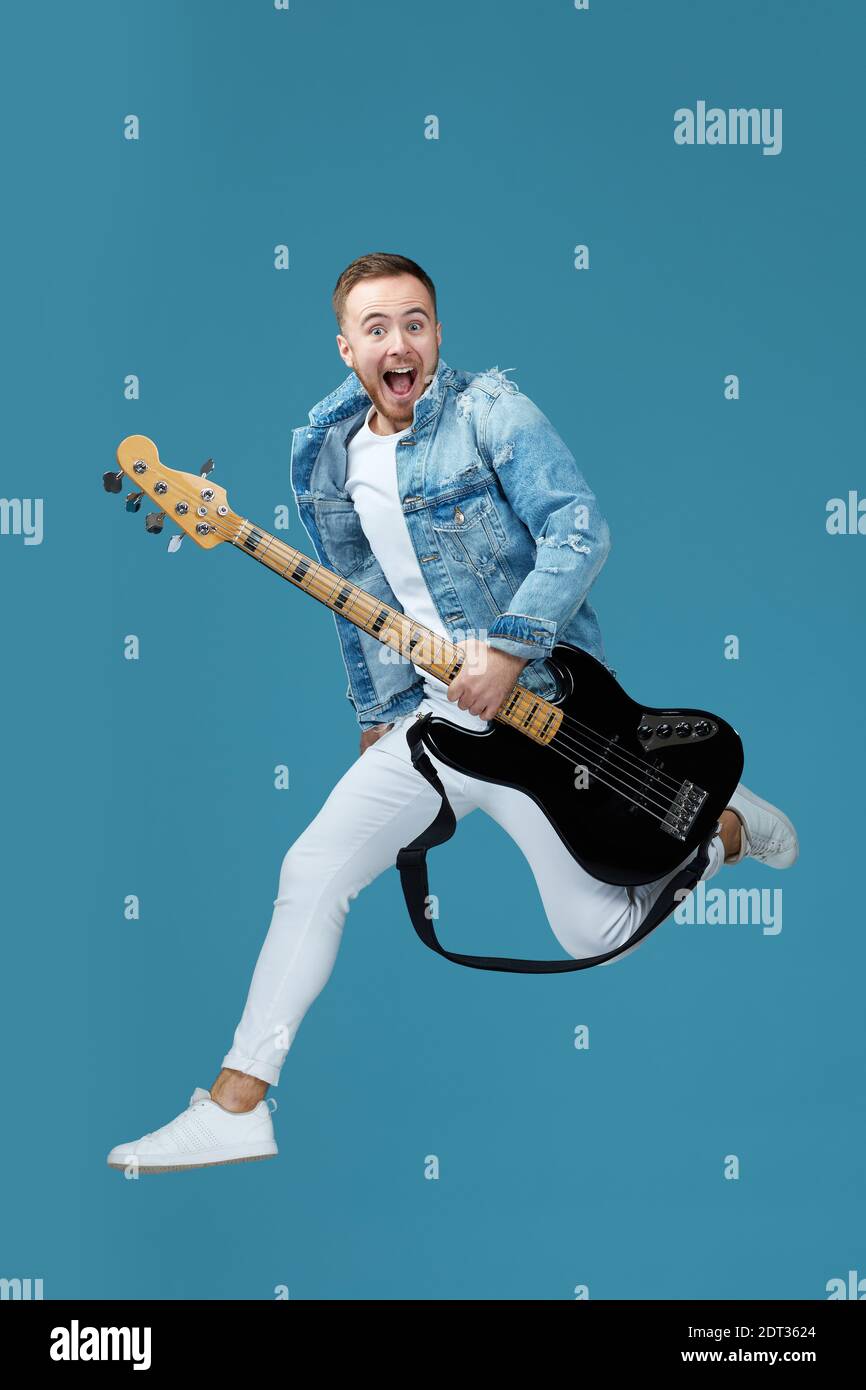 beau homme en jean t-shirt avec la guitare saut haut isolé sur fond bleu Banque D'Images