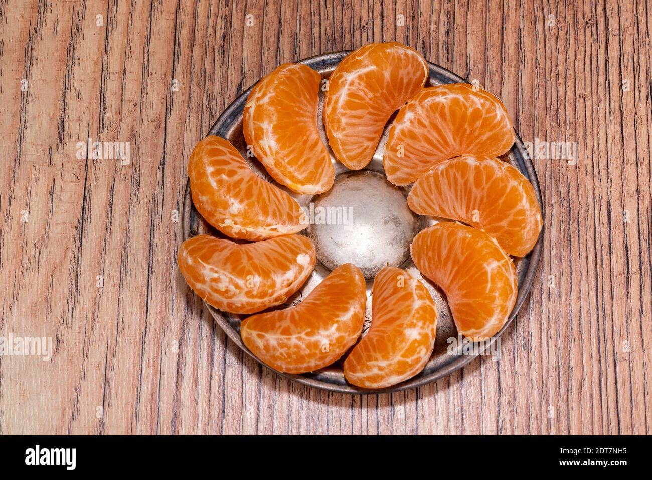 Les tranches de mandarine, soigneusement disposées sur une soucoupe en bronze, reposent sur une table en bois Banque D'Images