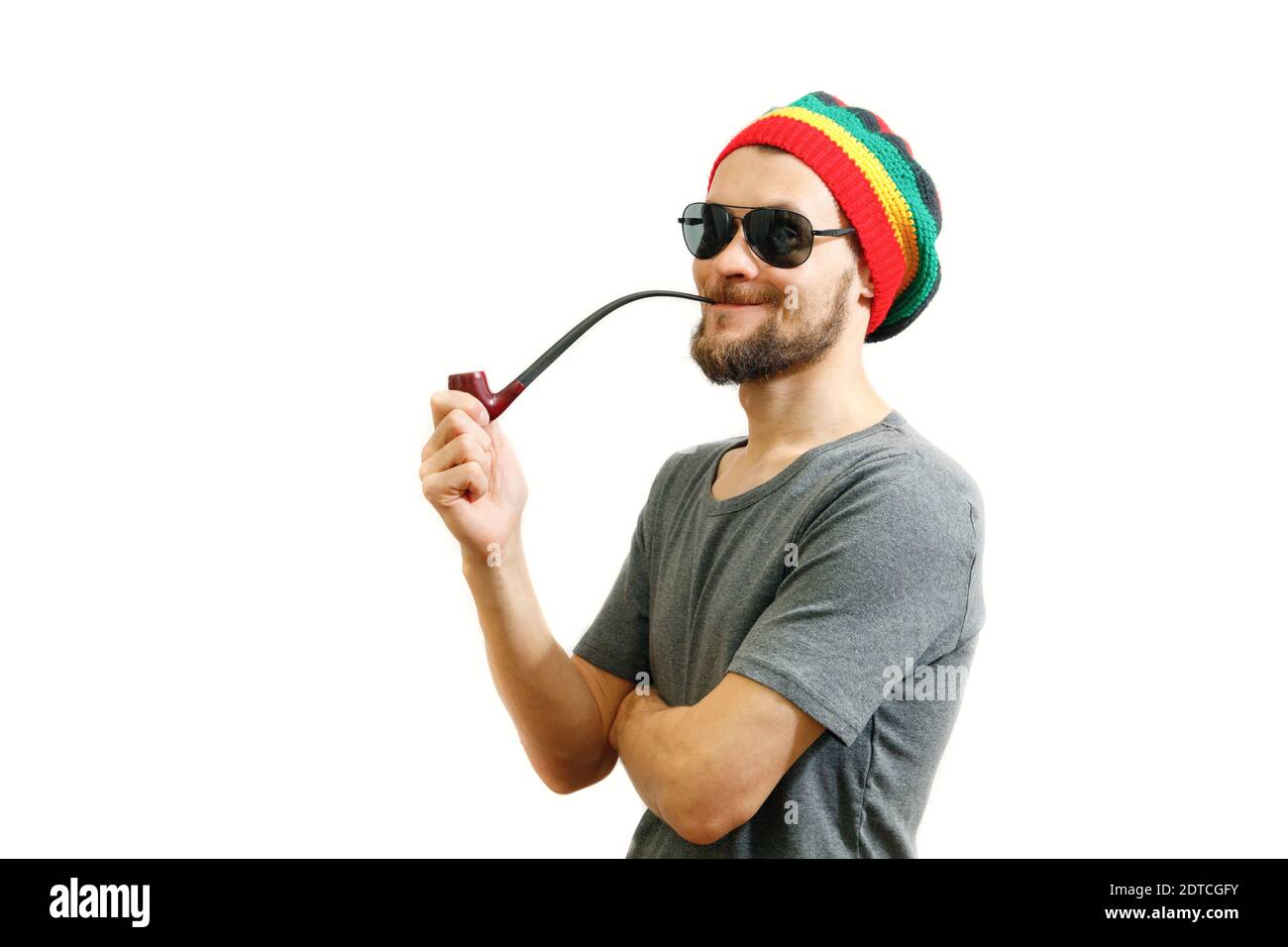 Jeune caucasien rasta en jamaïque chapeau, lunettes de soleil et t-shirt  gris sur fond blanc avec pipe de fumée en main Photo Stock - Alamy