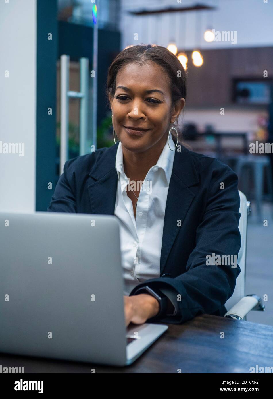 Smiling businesswoman working on laptop at desk in office Banque D'Images