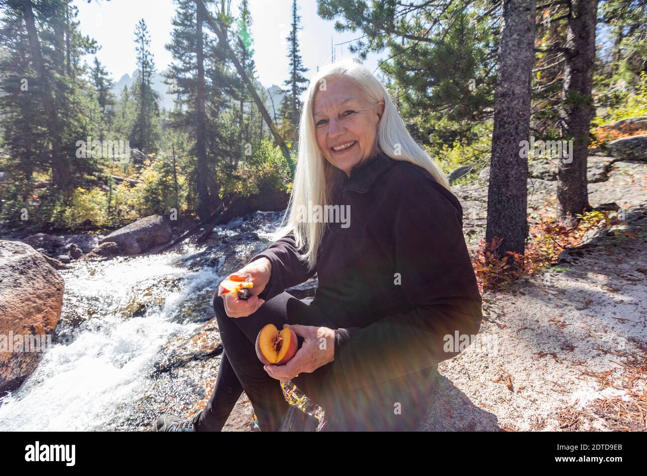 USA, Idaho, Stanley, randonneur senior souriant et coupant de la pêche fraîche à côté du ruisseau Banque D'Images