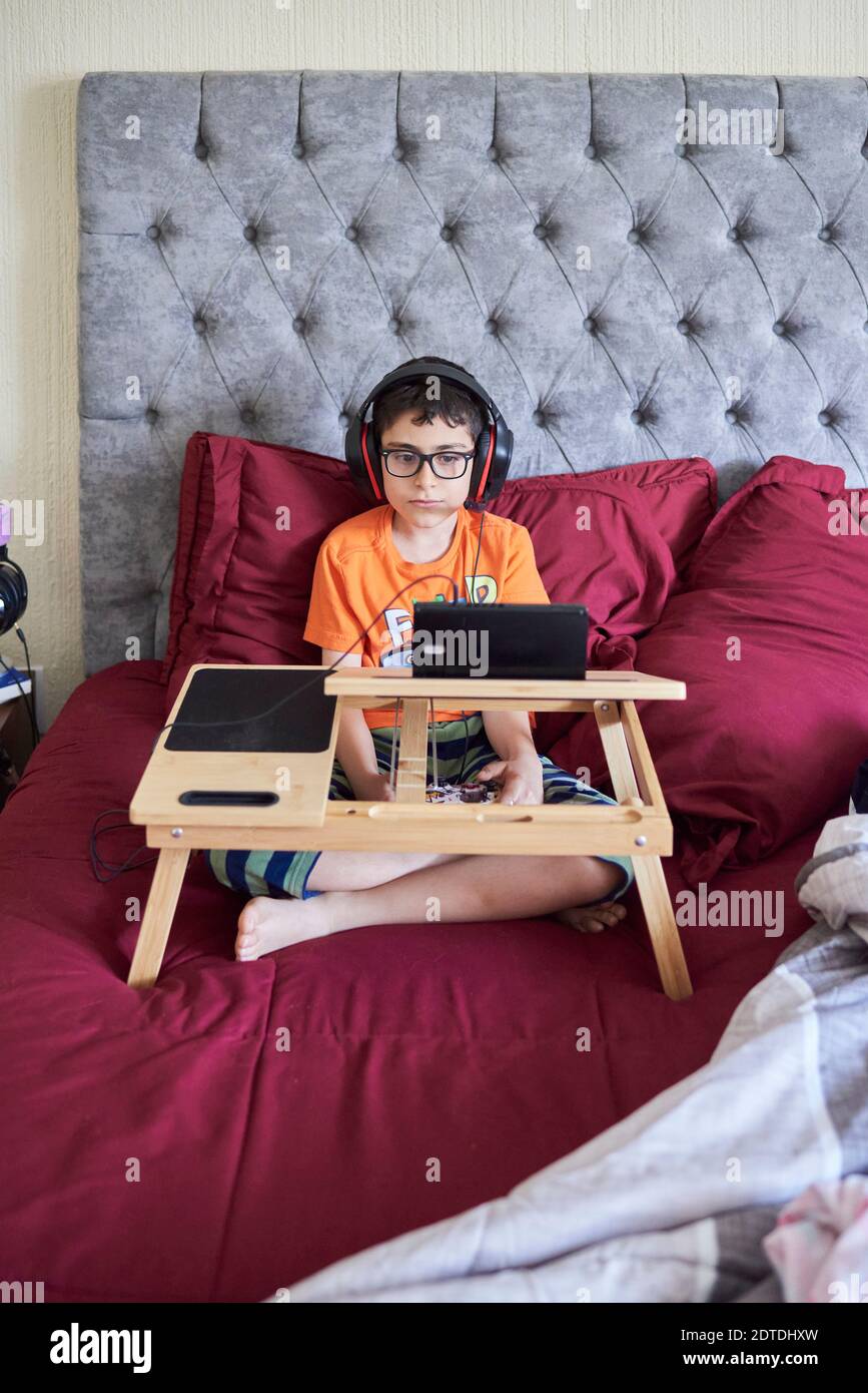 Garçon (8-9) jouant sur une tablette en étant assis au lit pendant week-end Banque D'Images