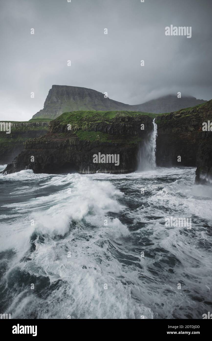 Danemark, îles Féroé, village de Gasadalur, cascade de MÂ·Lafossur, côte avec cascade de Mulafossur tombant dans l'océan Atlantique en temps de tempête Banque D'Images