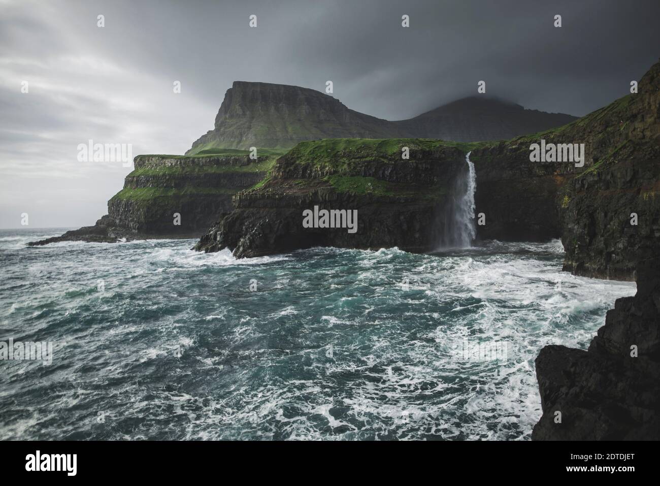 Danemark, îles Féroé, village de Gasadalur, cascade de MÂ·Lafossur, côte avec cascade de Mulafossur tombant dans l'océan Atlantique en temps de tempête Banque D'Images