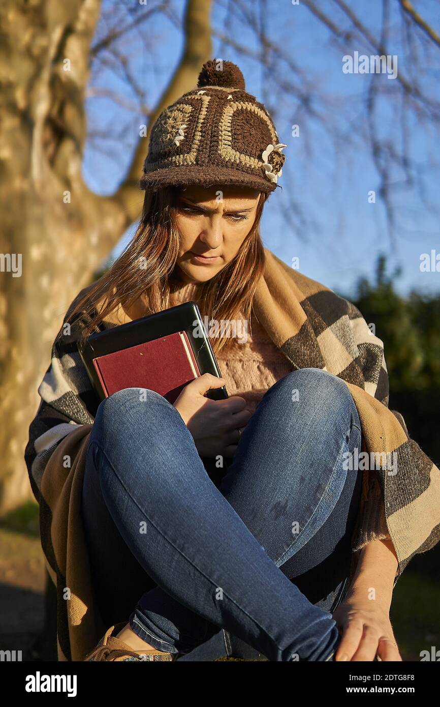 belle femme avec chapeau enfoncé assis dans un parc au coucher du soleil  avec ordinateur portable et livre Photo Stock - Alamy