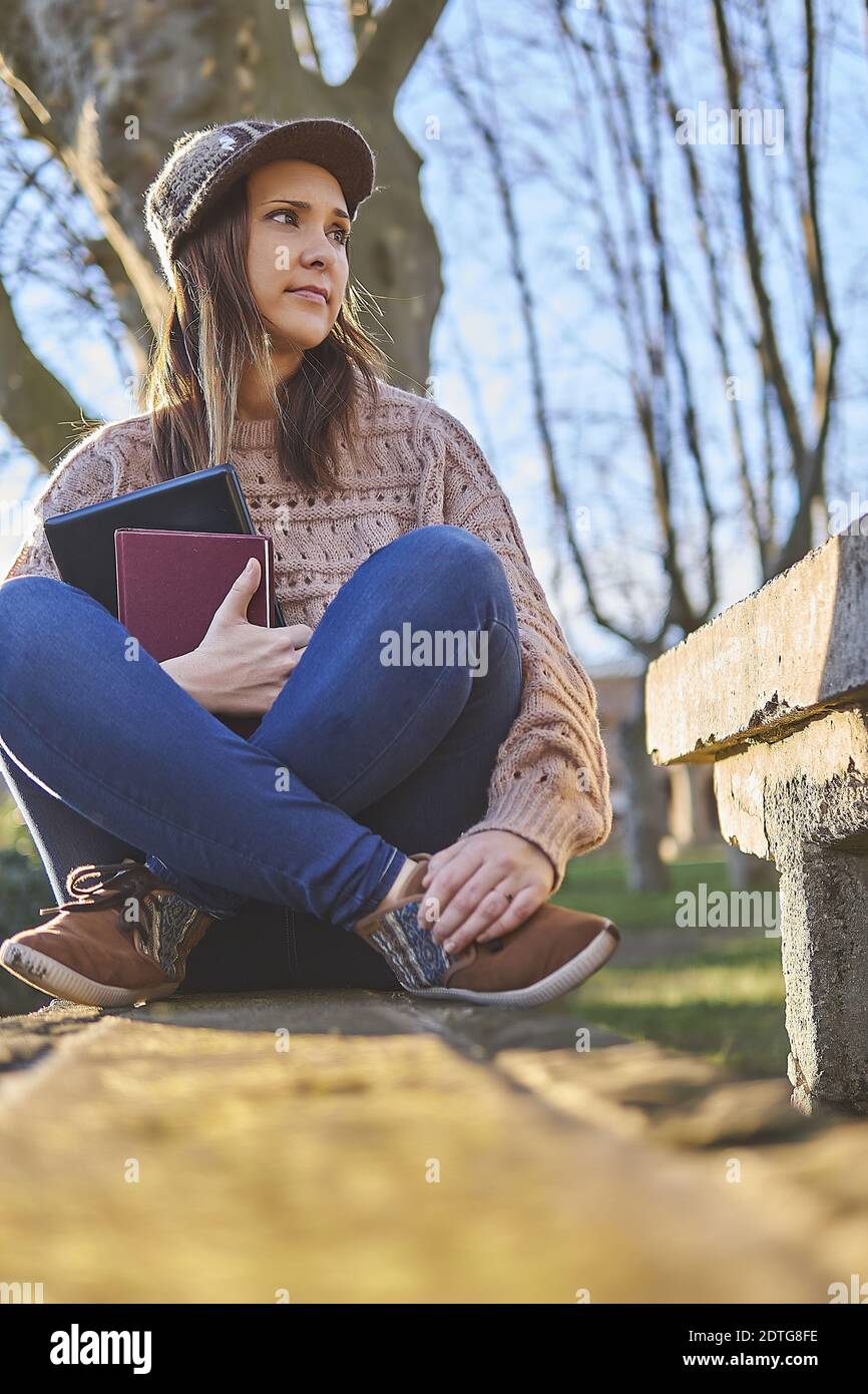 belle femme en chapeau enfoncé assis sur un banc de pierre dans le parc au  coucher du soleil avec ordinateur portable et livre. étudiant concept Photo  Stock - Alamy