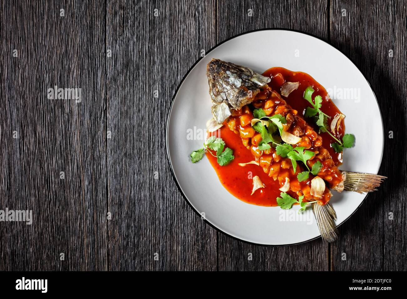 Écureuil de carpe de poisson aigre et sucré chinois avec cilantro frais servi sur une assiette sur fond de bois foncé, vue de dessus, espace de copie, gros plan Banque D'Images