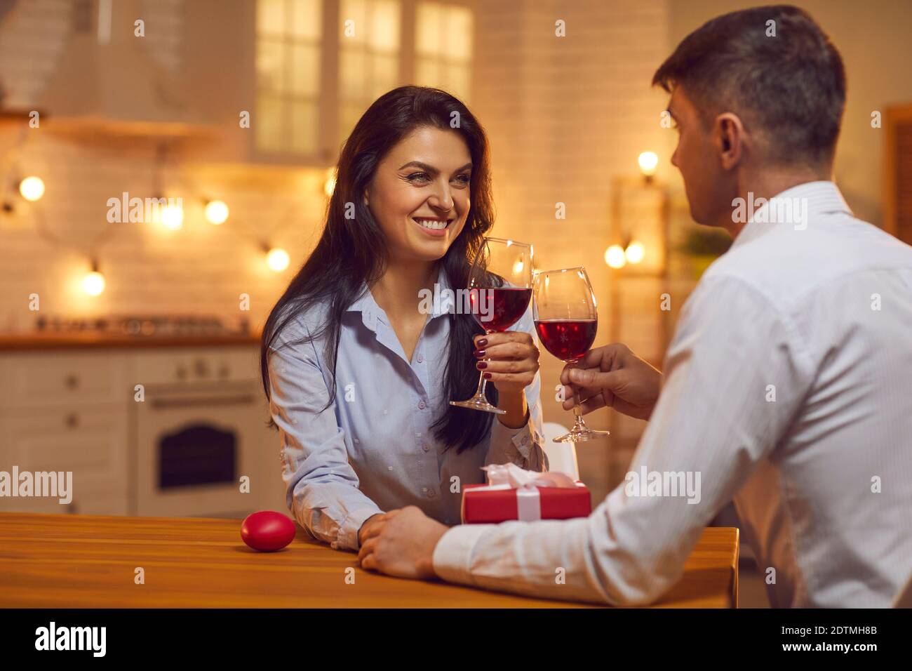 Jeune couple aimant assis ensemble dans la cuisine, tenant les mains, buvant du vin pendant la Saint Valentin Banque D'Images
