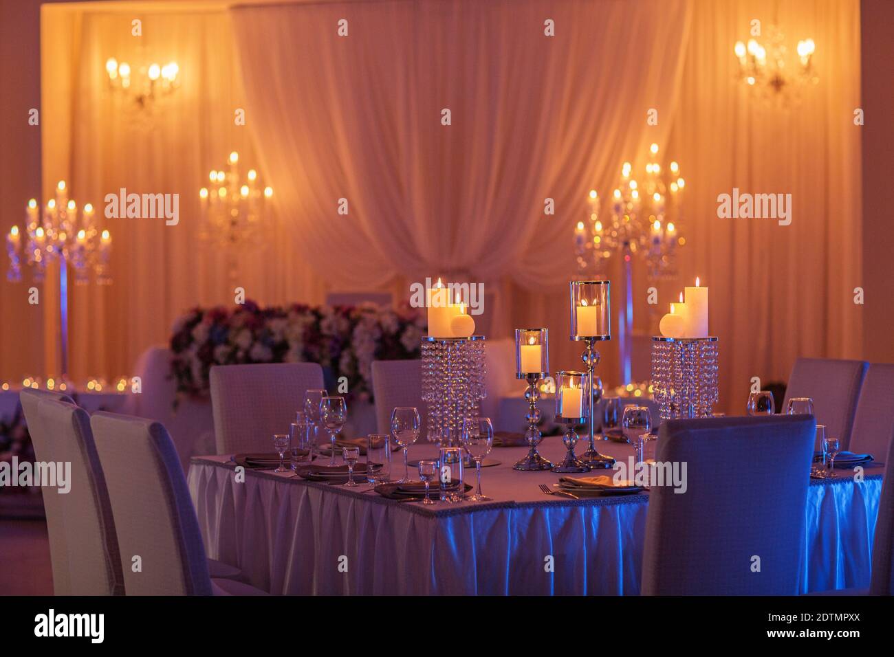 table de mariage festive avec bougies, cristal, assiettes et verres en lumière jaune. Porte-bougie en cristal comme pièce centrale à la réception d'un mariage Banque D'Images