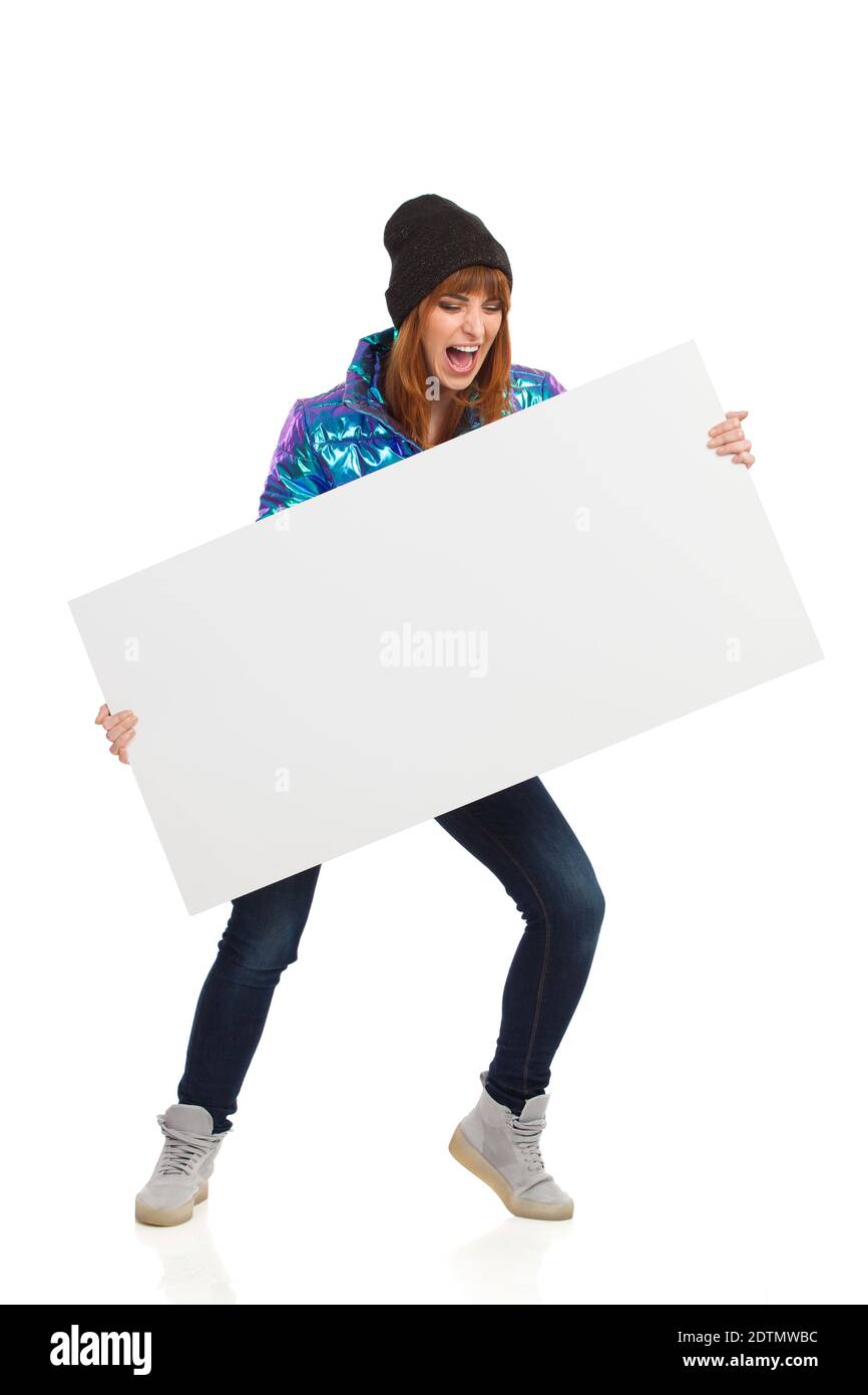 Crier une jeune femme dans des vêtements d'hiver tient une bannière blanche. Prise de vue en studio sur toute la longueur isolée sur blanc. Banque D'Images