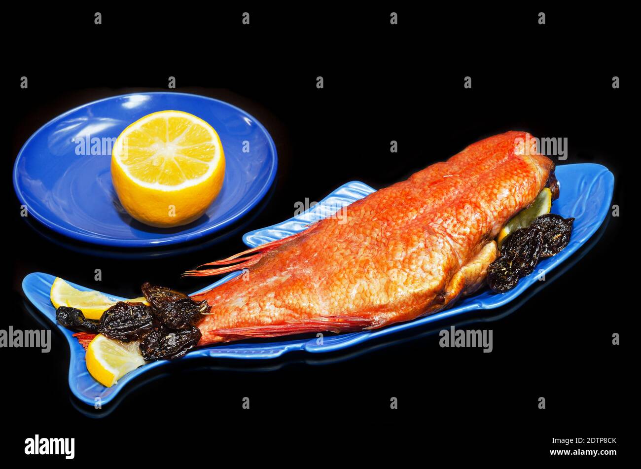 Bar chaud fumé avec citron et prunes épicées séchées, gros plan sur une assiette en forme de poisson et fond noir. Fruits de mer pour une bonne nutrition Banque D'Images