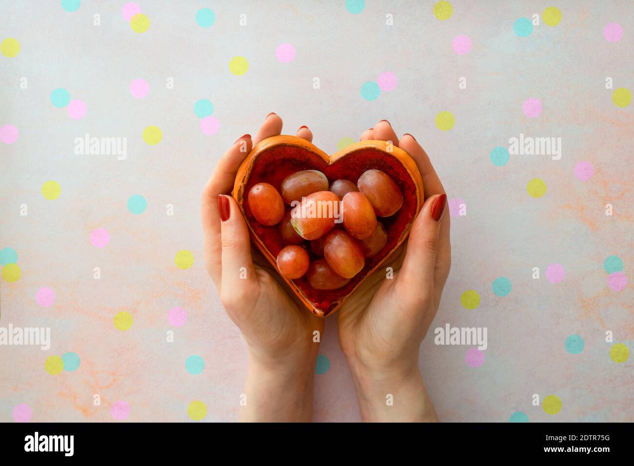 Bol en forme de coeur tenu par les mains des femmes avec des raisins consommés un par un à chaque coup de l'horloge de la Saint-Sylvestre en Espagne sur un fond de confetti. Banque D'Images