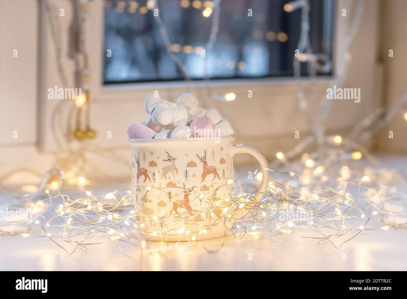 Guimauve dans une coupe de Noël. La coupe est située sur une fenêtre décorée d'une guirlande. Mise au point sélective. Banque D'Images