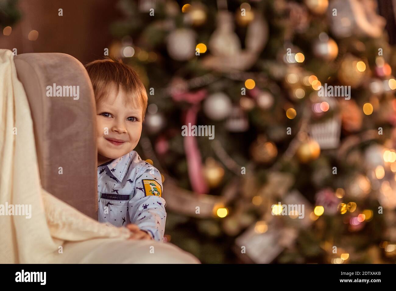 Un beau garçon de 4-5 ans se tient près du canapé et rêve de vacances et de cadeaux. Le concept des vacances d'hiver. Mise au point douce sélective, Banque D'Images