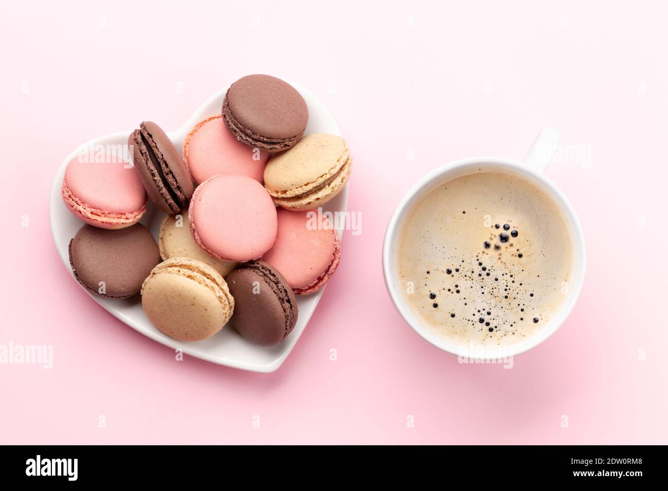 Saint-Valentin avec macarons dans une assiette en forme de coeur et une tasse de café sur fond rose. Plan d'étapage avec vue de dessus Banque D'Images