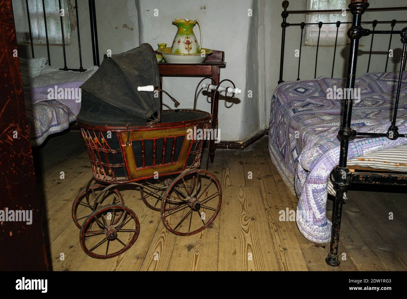 Poussette ancienne vintage pour bébé dans une chambre sombre de style ancien, avec deux lits anciens et des couvertures Banque D'Images