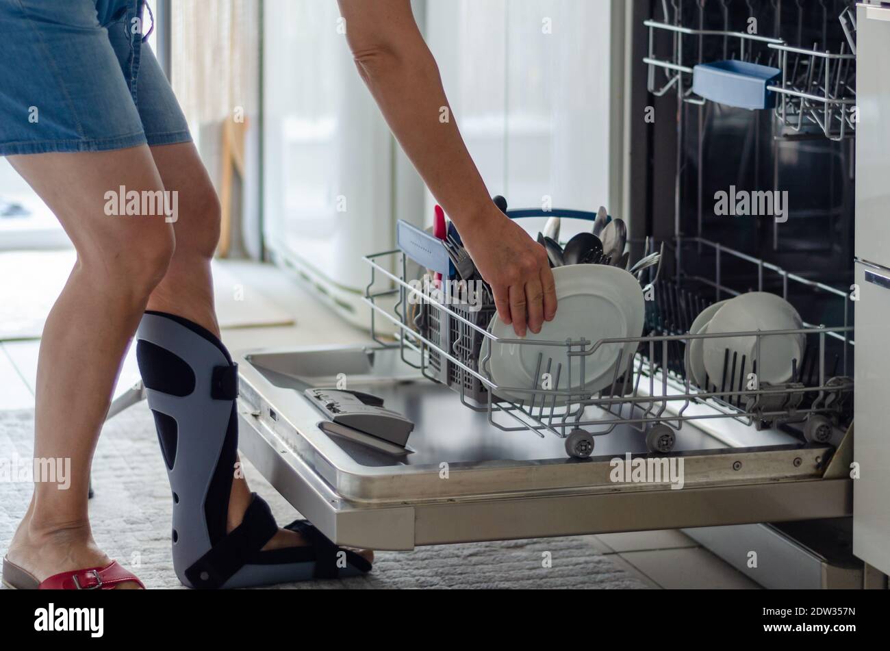 La Femme Avec Une Orthèse Sur Son Pied Se Vide Le Lave-Vaisselle Dans La  Cuisine Photo Stock - Alamy